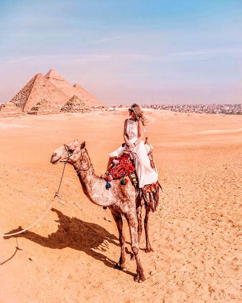 A woman in a white dress riding a camel with the pyramids in the background, symbolizing travel connectivity in Egypt.