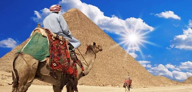 A traveler riding a camel with the Giza Pyramids in the background under a bright sky.