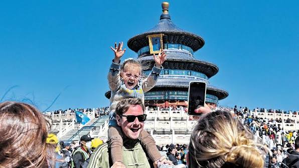 Father carrying child on shoulders, both smiling at the Temple of Heaven in Beijing