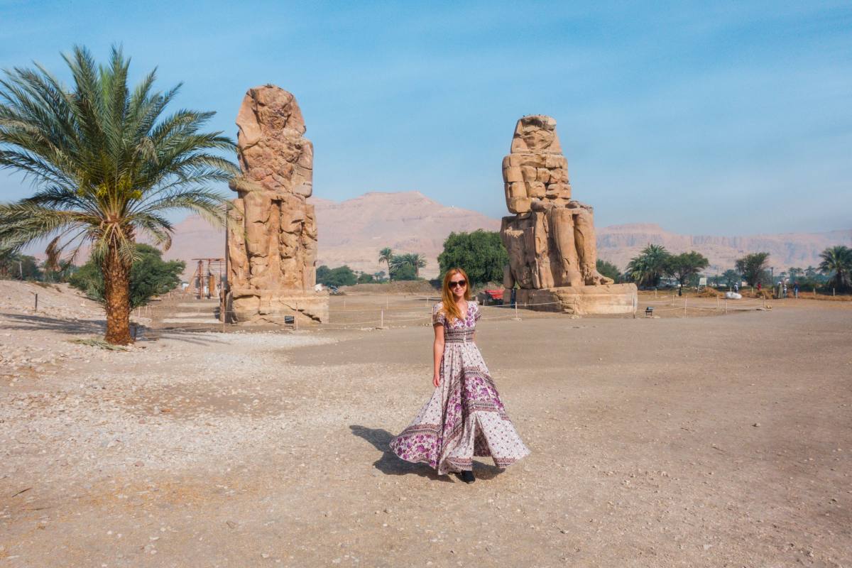 Una donna in abito lungo si trova tra i Colossi Memnone di Luxor, Egitto.