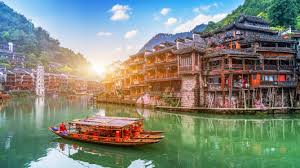 A traditional boat on a river in a scenic Chinese water town with ancient buildings and lush mountains.