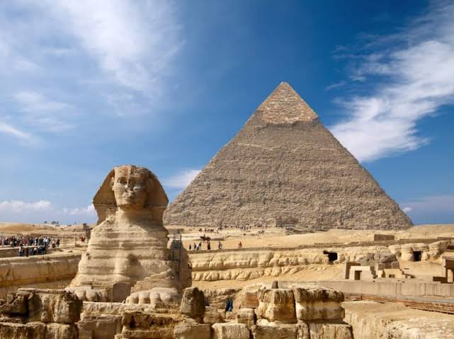Ancient Egyptian pyramids and the Sphinx under a clear blue sky, with tourists in the distance.